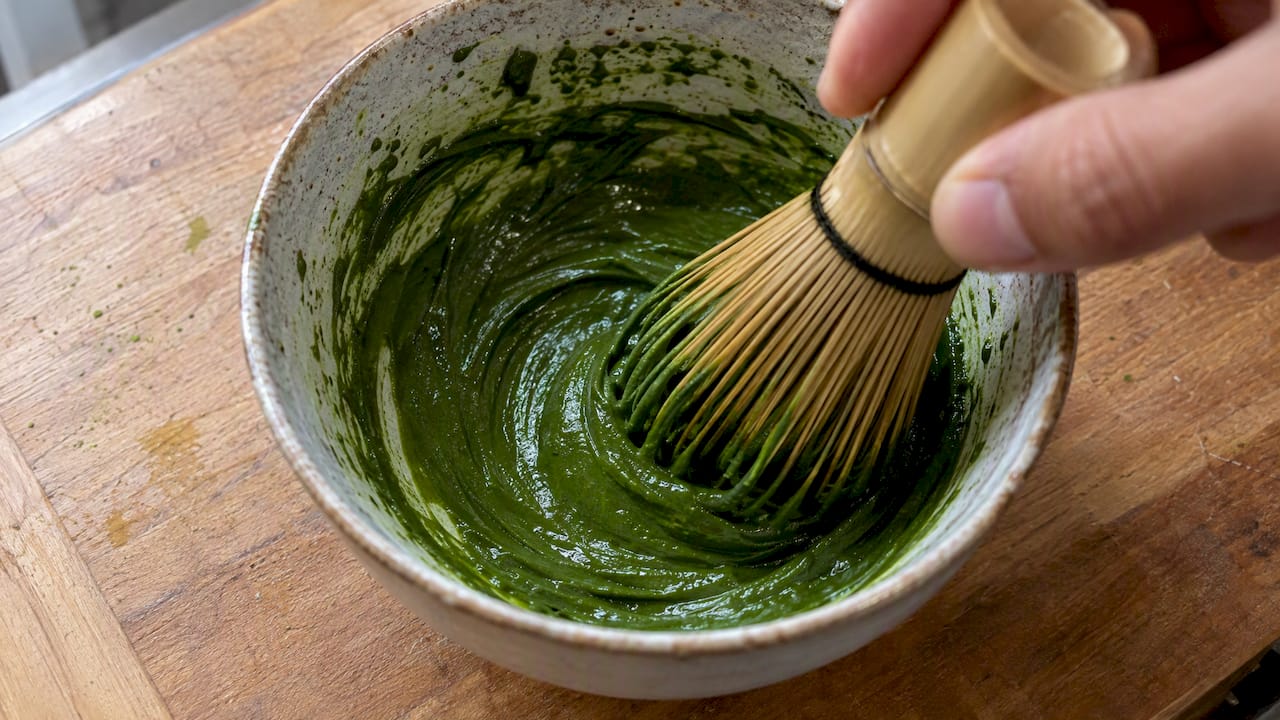 Fouet en bambou plongé dans une pâte lisse au matcha