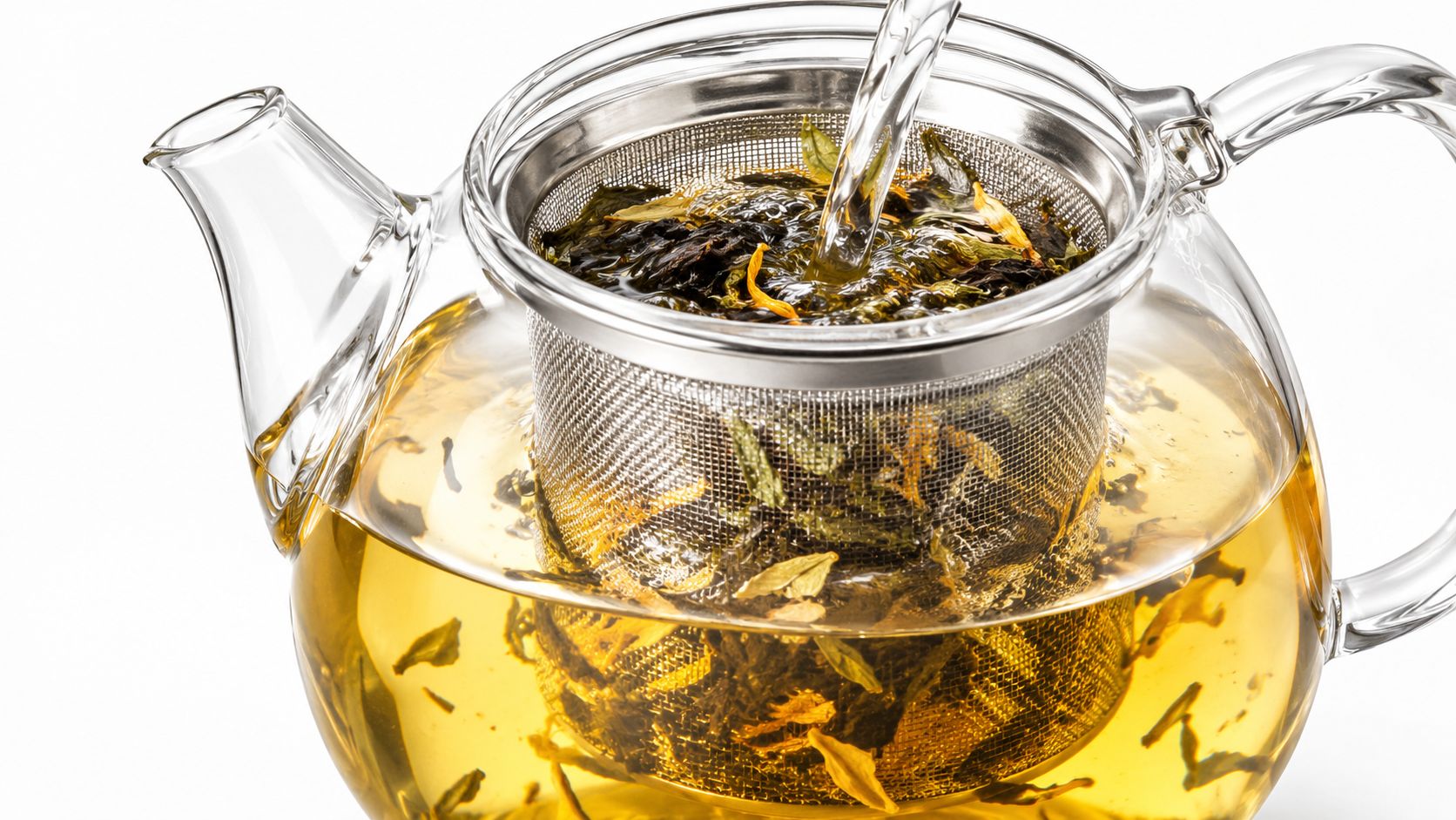 Hot water pouring into a clear glass teapot with a metal infuser basket filled with tea leaves.